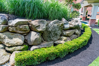 Multi-tiered natural stone boulder waterfall cascading into a pool surrounded by lush landscaping
