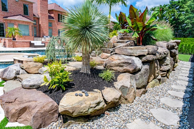 Multi-tiered natural stone boulder waterfall cascading into a pool surrounded by lush tropical plants