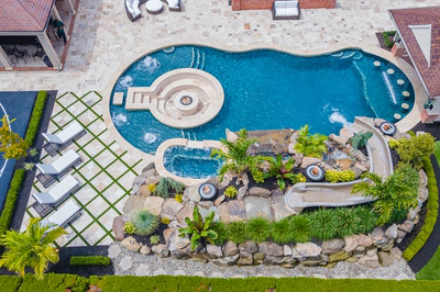 Multi-tiered natural stone boulder waterfall cascading into a freeform pool surrounded by tropical plants