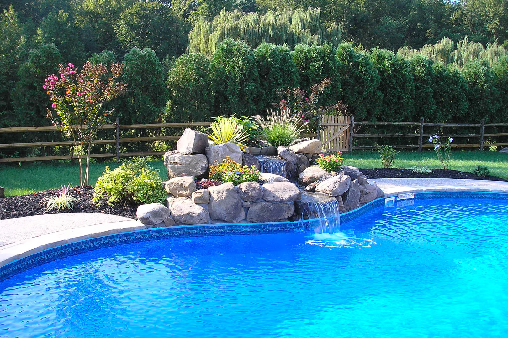 Natural stone boulder waterfall cascading into a pool surrounded by lush garden plants