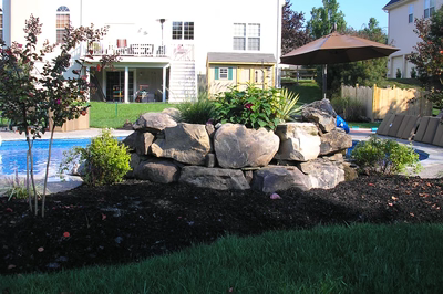 Two-tiered natural stone boulder waterfall cascading into a pool surrounded by lush garden plants