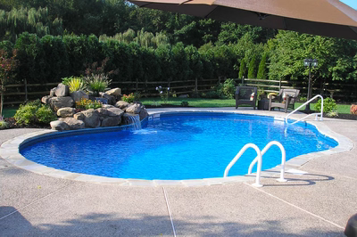 Multi-tiered natural stone boulder waterfall cascading into a blue pool surrounded by lush garden plants