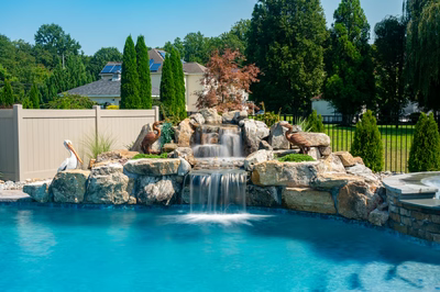 Multi-tiered natural stone boulder waterfall cascading into a pool with decorative statues and lush greenery