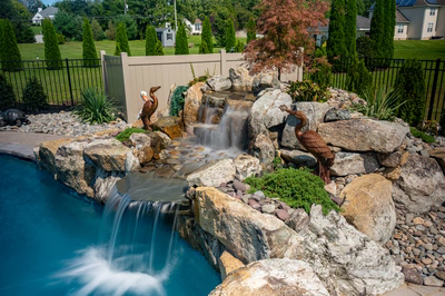 Three-tiered natural stone boulder waterfall cascading into a pool surrounded by lush garden plants