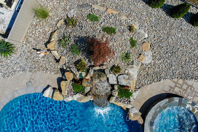 Single-tiered natural stone boulder waterfall cascading into a pool surrounded by gravel and greenery