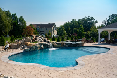 Multi-tiered natural stone boulder waterfalls cascade into a freeform pool surrounded by lush greenery