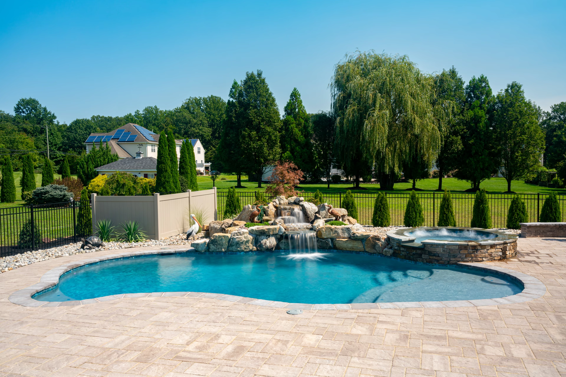 Two-tiered natural stone boulder waterfall cascading into a freeform pool with surrounding lush landscaping