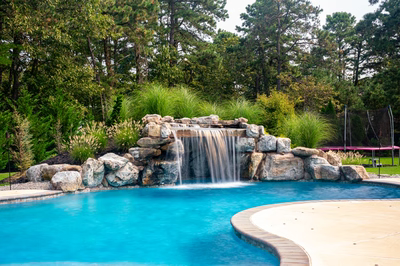 Single-tier natural stone boulder waterfall featuring curtain flow spilling into a pool with lush greenery