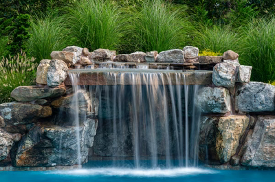 Two-tiered natural stone boulder waterfall cascading into a pool surrounded by lush ornamental grasses