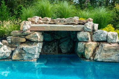 Single-tier natural stone boulder waterfall cascading into a pool with lush ornamental grasses