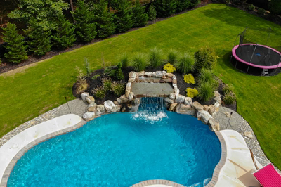Two-tiered natural stone boulder waterfall cascading into a freeform pool with lush landscape plantings