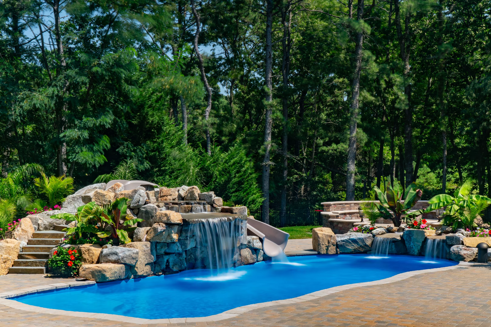 Cascading stone boulder waterfall flowing into a freeform pool with lush tropical plants