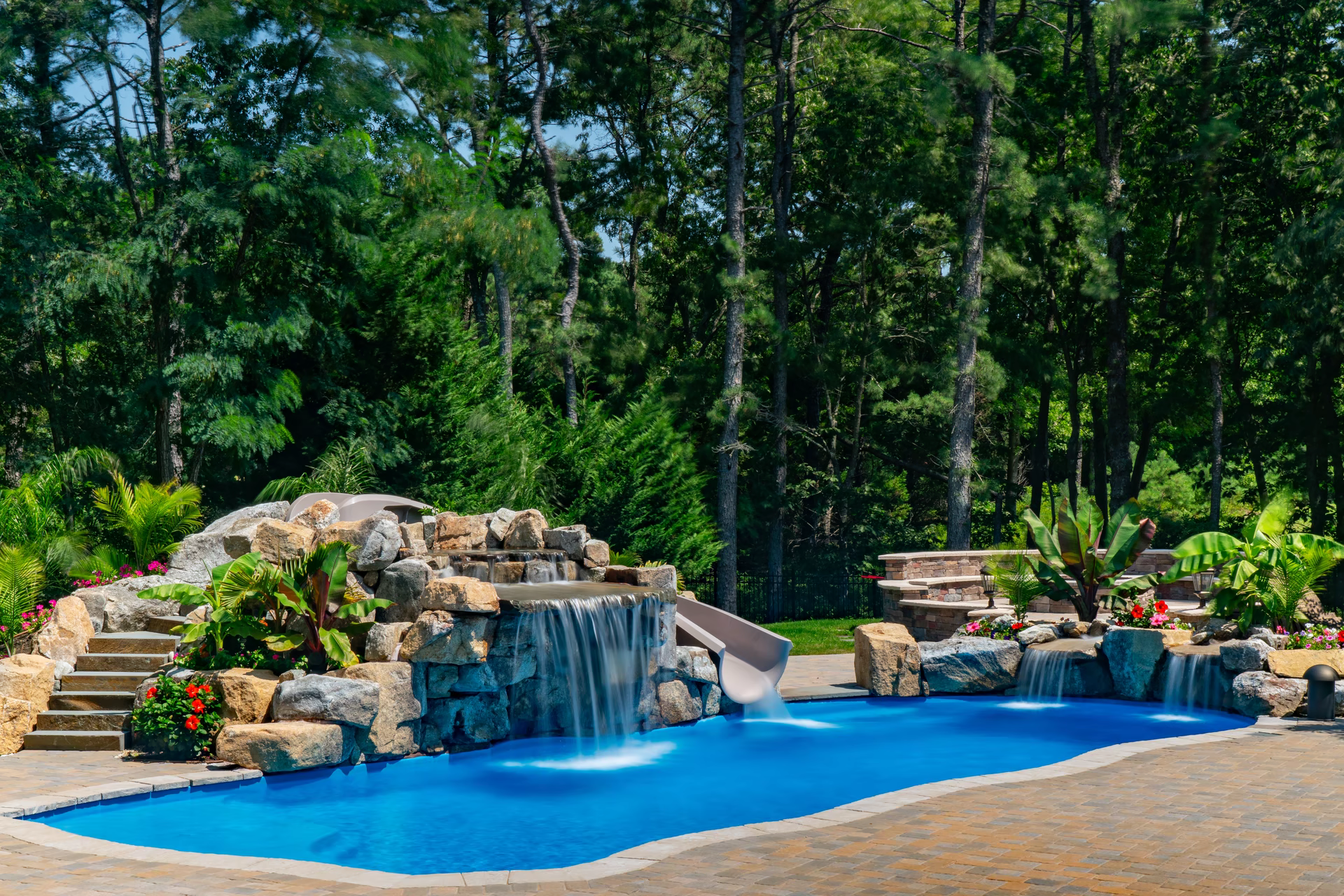 Cascading multi-tiered stone boulder waterfall flowing into a freeform pool with lush tropical plants