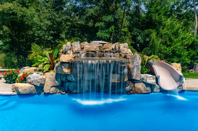Two-tiered natural stone boulder waterfall cascading into a blue pool with lush greenery