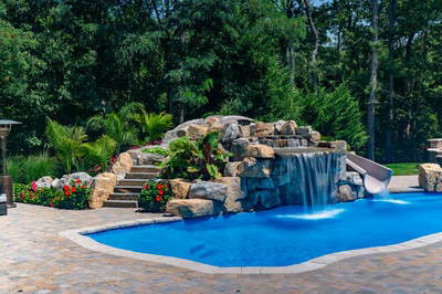 Two-tiered natural stone boulder waterfall cascading into a blue pool with tropical landscaping