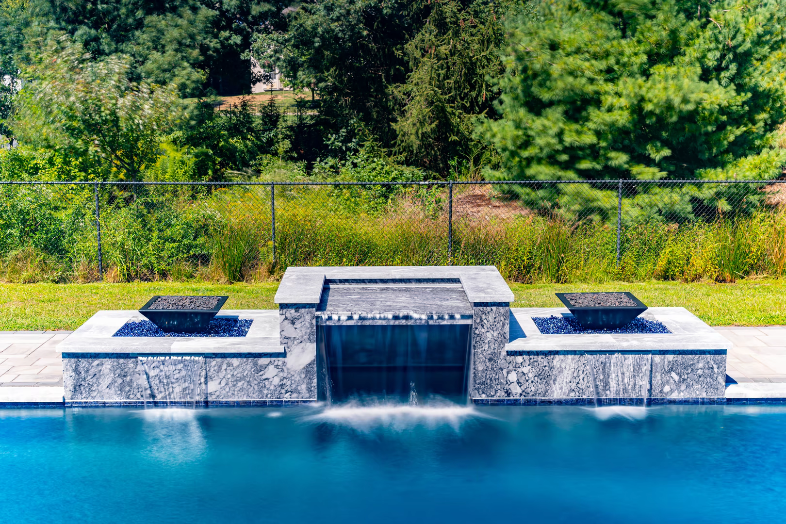 Stone waterfall cascading into a rectangular pool surrounded by lush green woodland landscaping