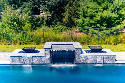 Three-tiered stone waterfall cascading into a rectangular pool surrounded by lush green woodland landscaping