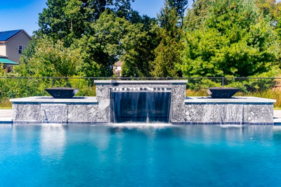 Three-tiered natural stone waterfall feature cascading into a pool with lush green surroundings