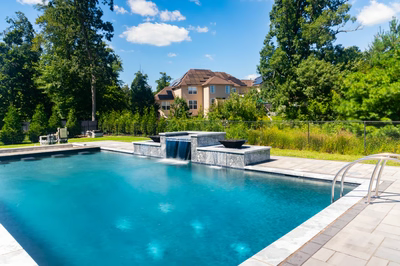 Three-tiered natural stone boulder waterfall cascading into a rectangular pool surrounded by lush greenery