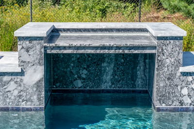 Two-tiered natural stone sheer descent waterfall cascading into a pool with lush landscaping