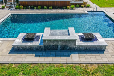 Modern three-tiered stone spillway with fire pits cascading into a rectangular swimming pool