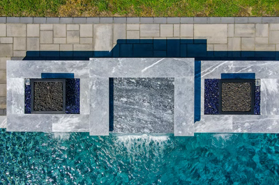 Single-tier natural stone spillway waterfall cascading into blue pool with geometric patio pavers