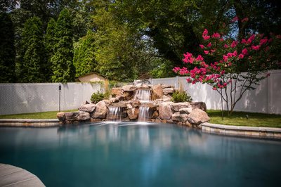 Two-tiered natural stone boulder waterfall cascading into a pool beside vibrant pink flowering trees