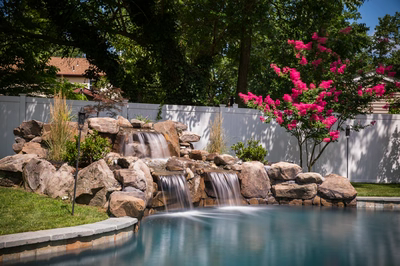 Multi-tiered natural stone boulder waterfall cascading into a pool surrounded by lush garden plants