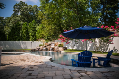 Multi-tiered natural stone boulder waterfall cascading into a pool surrounded by lush garden landscaping