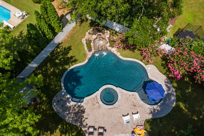 Two-tiered natural stone boulder waterfall cascading into a freeform pool surrounded by lush greenery