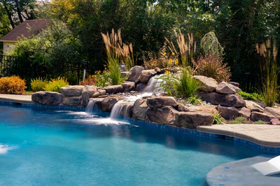 Multi-tiered natural stone boulder waterfall cascading into a pool surrounded by lush ornamental plants