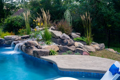 Two-tiered natural stone boulder waterfall cascading into a pool surrounded by ornamental grasses and plants