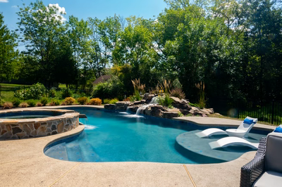 Multi-tiered natural stone boulder waterfall cascading into a freeform pool with lush, green landscaping