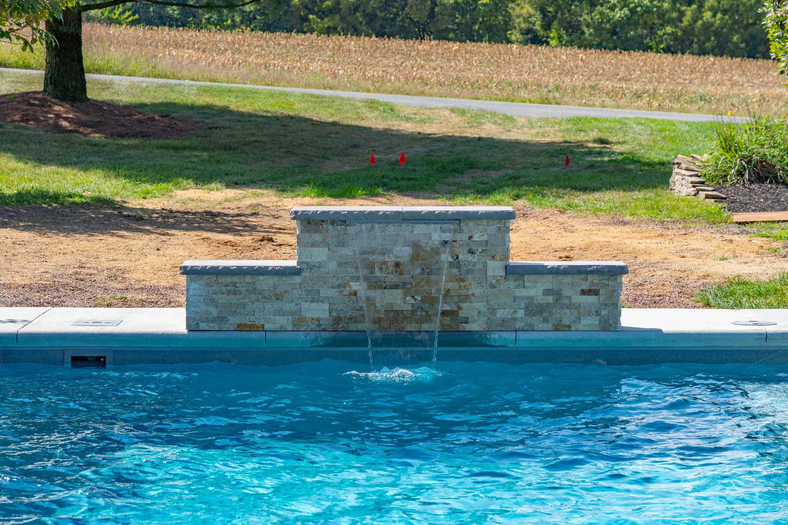 Natural stone waterfall cascading into a pool with lush green lawn and trees