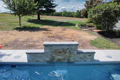 Three-tiered natural stone boulder waterfall creates sheer descent flow into pool with surrounding trees