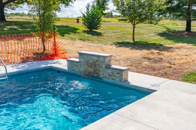 Three-tiered natural stone waterfall cascading into a blue pool surrounded by trees and lawn