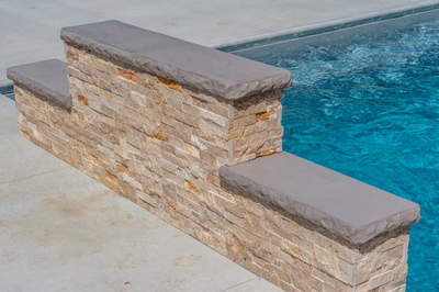 Three-tiered natural stone boulder waterfall cascading into a swimming pool beside a concrete deck