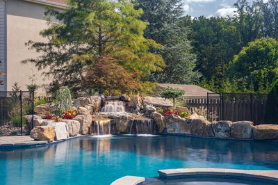 Three-tiered natural stone boulder waterfall cascading into a pool surrounded by lush garden plants