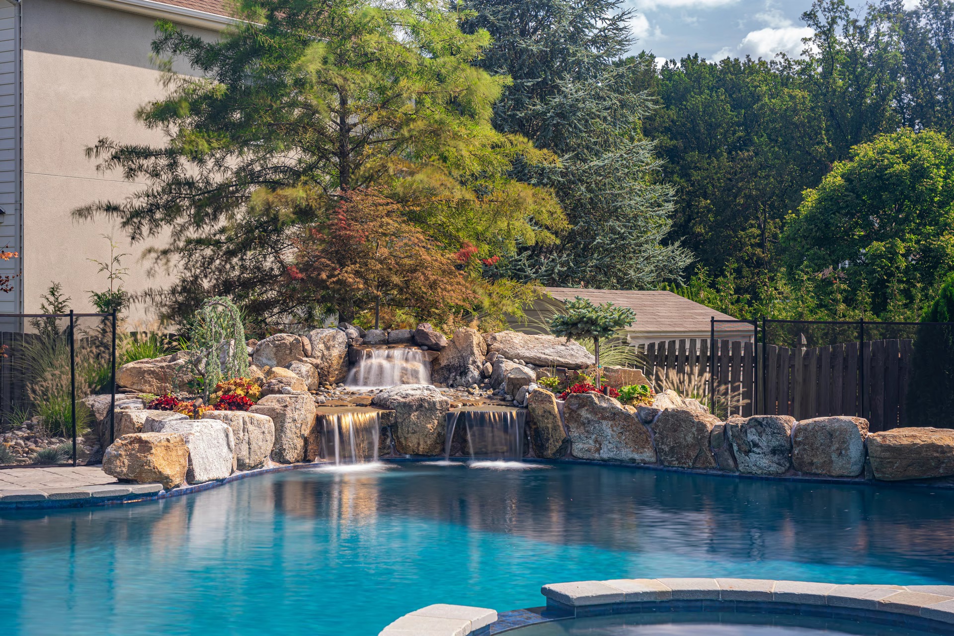 Three-tiered natural stone boulder waterfall cascading into a pool surrounded by lush garden plants