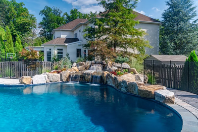Three-tiered natural stone boulder waterfall cascading into a pool surrounded by lush garden plants