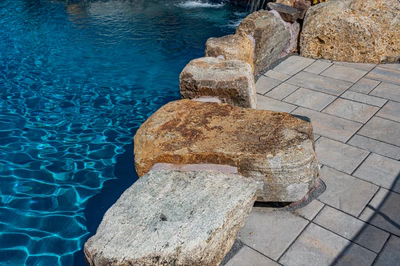 Multi-tiered natural stone boulder waterfall cascading into a pool with stone pavers and landscaping