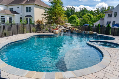 Multi-tiered cascading natural stone boulder waterfall flowing into a freeform pool with lush landscaping