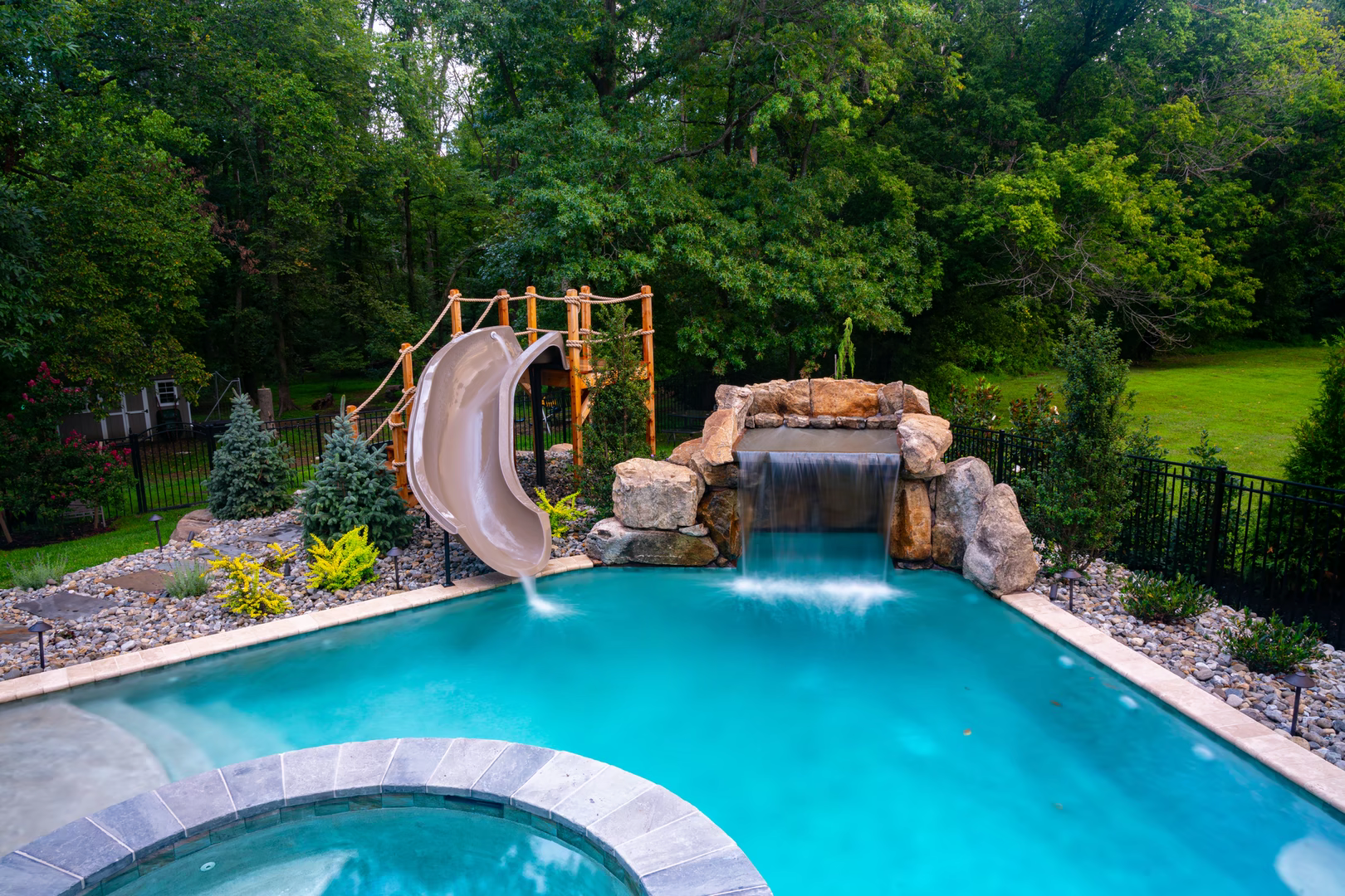 Natural stone boulder waterfall with sheet flow cascading into a pool near greenery