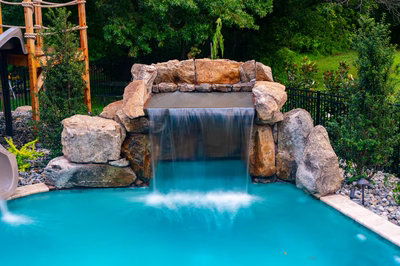 Multi-tiered natural stone boulder waterfall cascading into a pool surrounded by lush green foliage