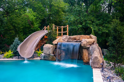 Multi-tiered natural stone boulder waterfall cascades into a pool surrounded by lush garden foliage