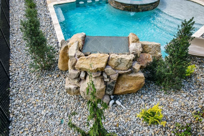 Two-tiered natural stone boulder waterfall cascading into a pool surrounded by lush green trees