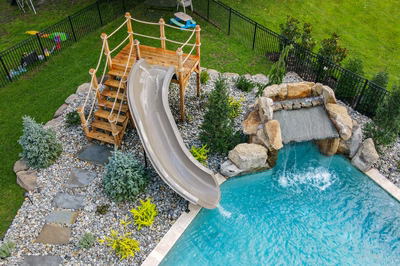 Single-tier natural stone boulder waterfall with sheet flow cascading into pool surrounded by lush greenery