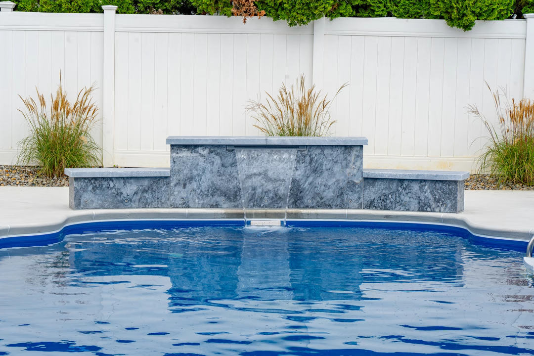 Three-tiered natural stone boulder waterfall cascading into a blue pool with surrounding ornamental grasses