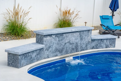 Three-tiered natural stone boulder waterfall cascading into pool with surrounding ornamental grasses