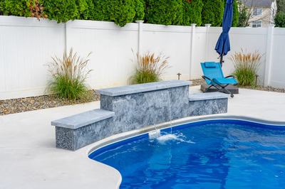 Three-tiered natural stone waterfall cascading sheer flow into pool near lush ornamental grasses